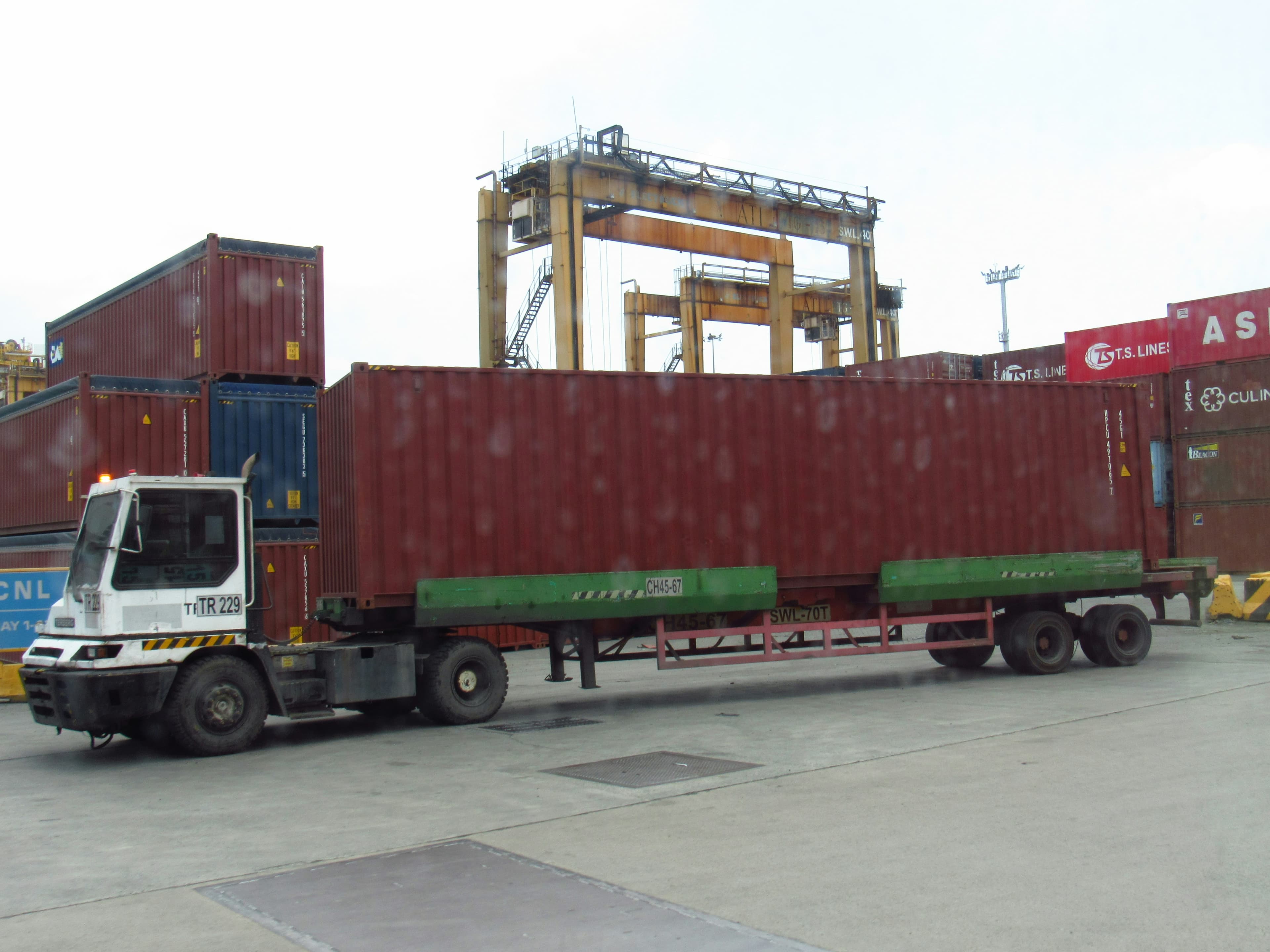 A truck carrying a large shipping container at a port.